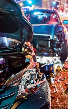Two damaged cars requiring auto body accident repair at a night-time scene with debris scattered on the road.