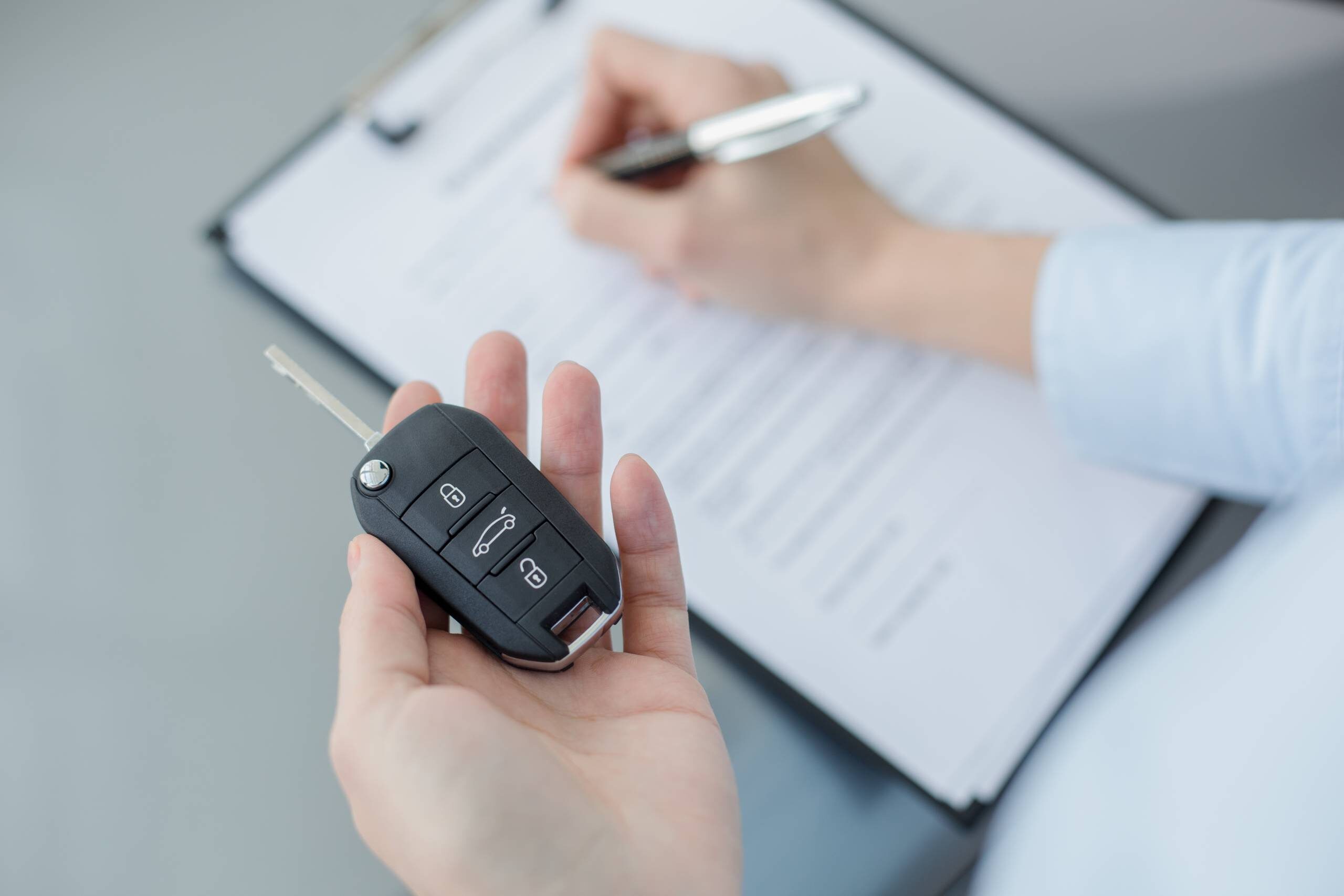 A person signs an accident repair document on a clipboard while holding a car key fob.