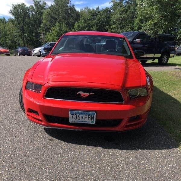 A red Ford Mustang parked on an asphalt lot, showing Minnesota license plate 736 PBN, after undergoing collision repair.