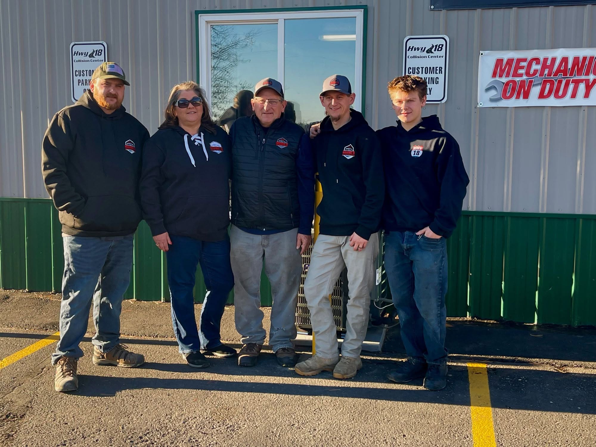 Five people stand in a line outside an auto body repair shop.